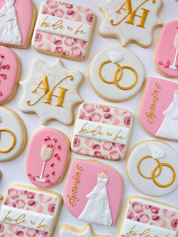 Hand-decorated wedding-themed cookies with gold and pink designs on a white background