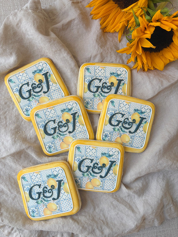 Square cookies with a detailed fabric pattern background and initials G & J